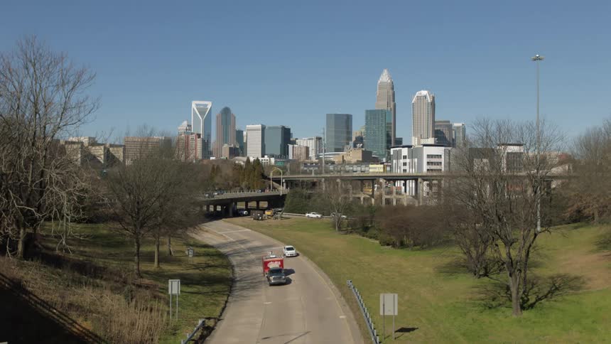 A city skyline with buildings and skyscrapers with a road with vehicles in the foreground and the sky and clouds in the background