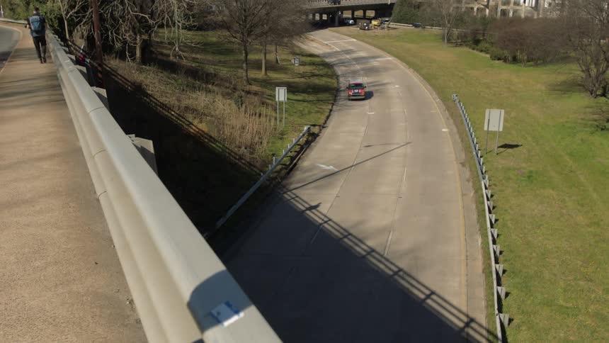 A man walks along the sidewalk on a bridge as vehicles pass below him