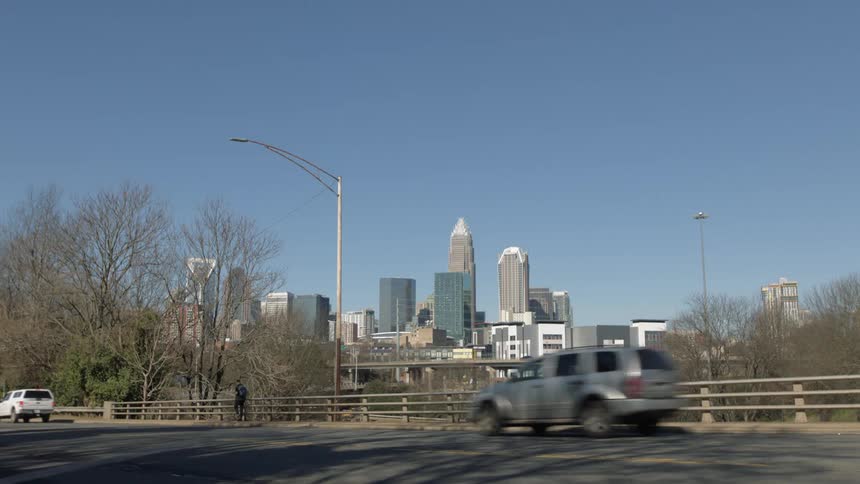 Cars and a truck travel on a city road as a pedestrian walks on the sidewalk