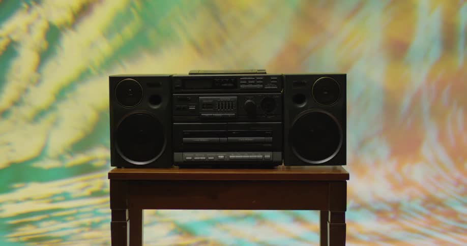 Colorful lights and images swirl behind a boombox on a wooden table