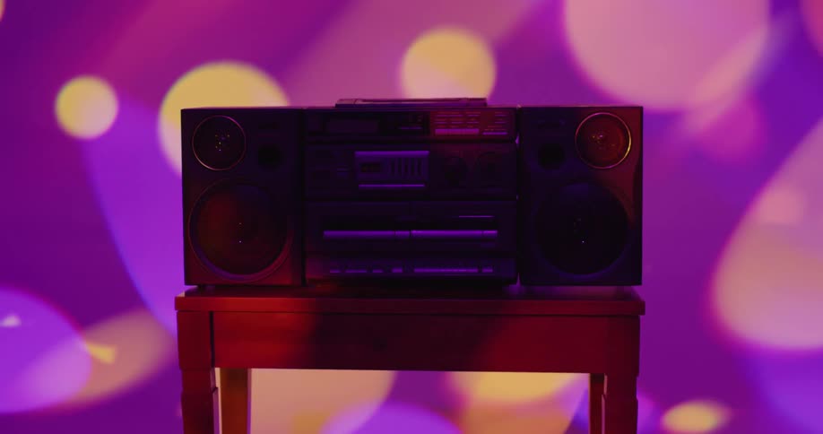 Vintage boombox resting over a wooden table inside a room under colorful moving lights