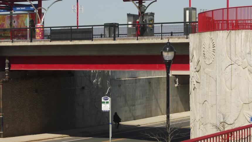 A man walks across an overpass from a train stop as a bicyclist rides under the bridge