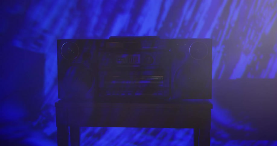 A boombox is located in a dark room while flashing lights illuminate the wall behind it