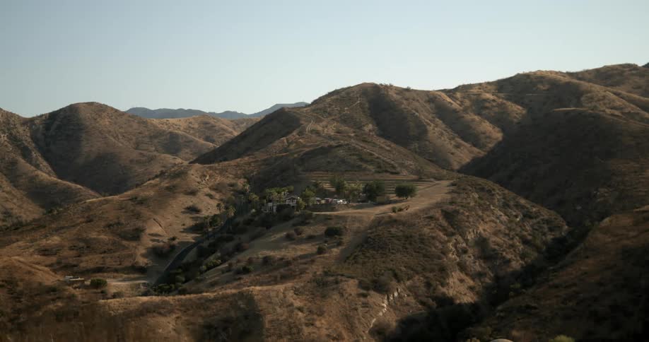 A house in the mountains and a mountain range in the distance under a clear sky