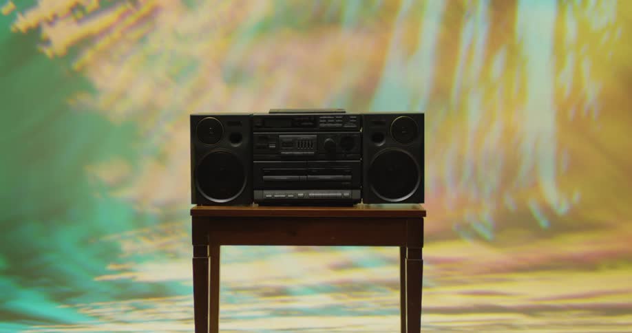 A boombox is located atop a small table while a light show is projected onto the wall behind it