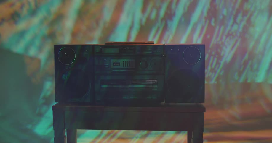 A boombox on a table in a room with a wall and a screen in the background