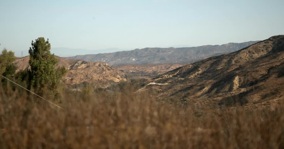 Mountains with a few trees nearby and a mountain range on the horizon