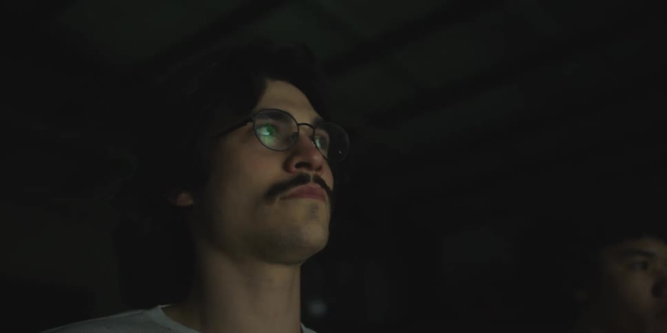 Man sits in audience watching movie in dark theater with projection room near ceiling behind him
