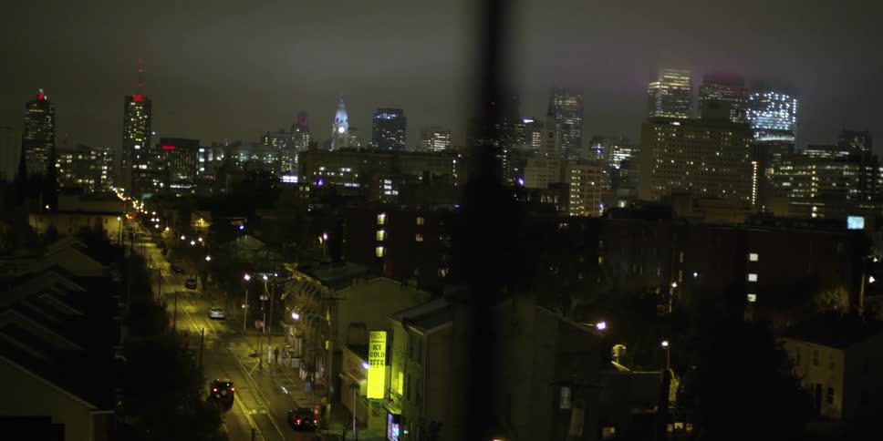 A city street and city are seen at night through a window