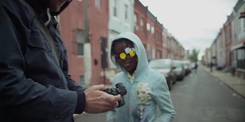 A man in a jacket hands a camera to a child in blue