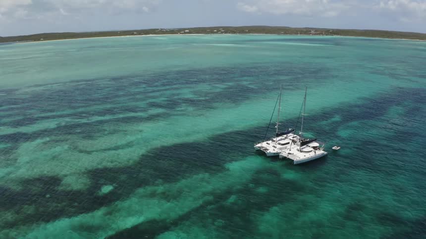 Two large sail boats are anchored next to each other in the shallows near to a sandy beach