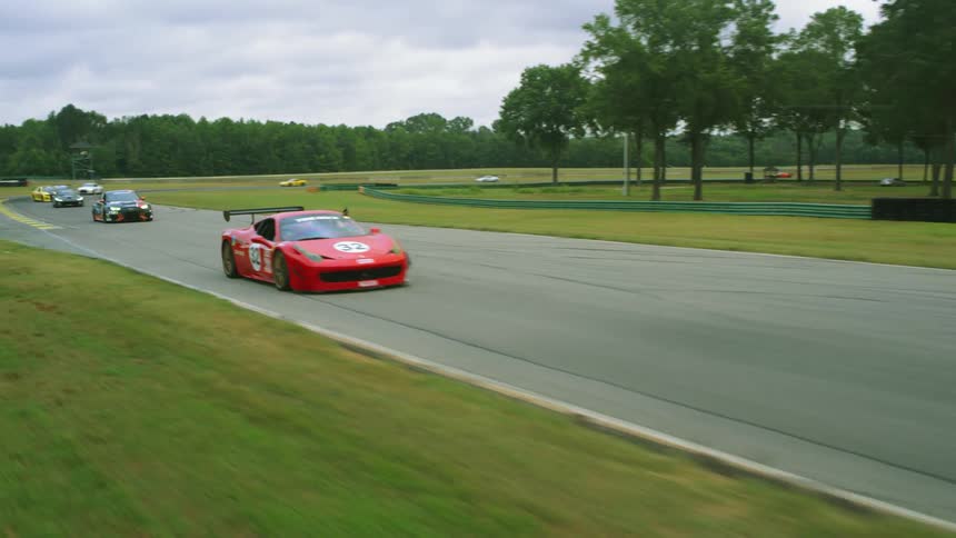 Race cars speed along race track with woods in background