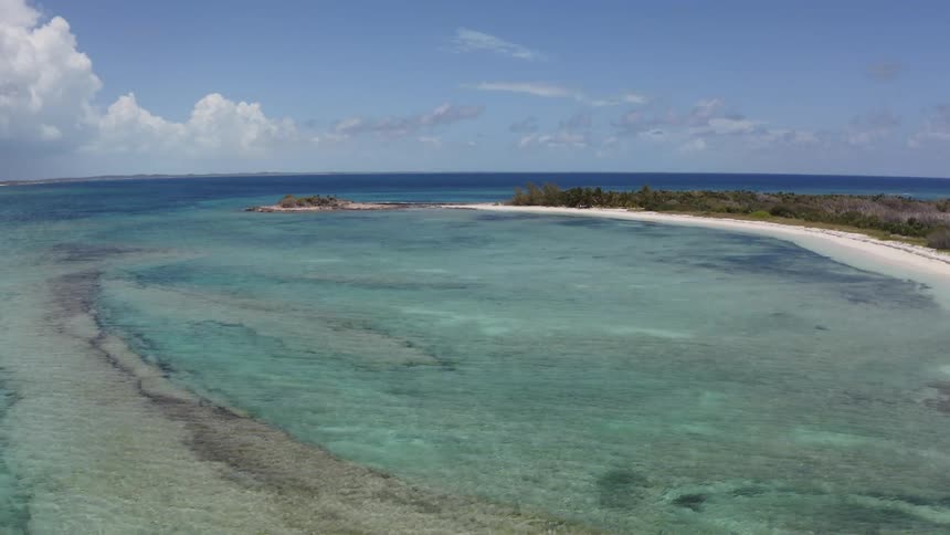 Clear blue water rolling onto a beach on a beautiful day with a few clouds in the sky
