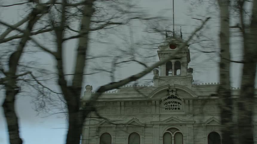 Leafless trees border architecturally detailed court house under overcast sky