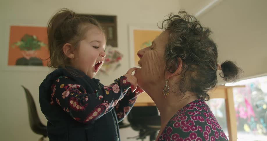 Granddaughter opens her mouth as she examines her grandmothers mouth and earrings