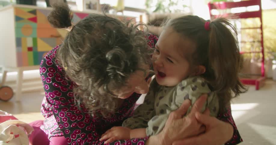 A woman gives her granddaughter a huge hug and kiss as they play in the living room