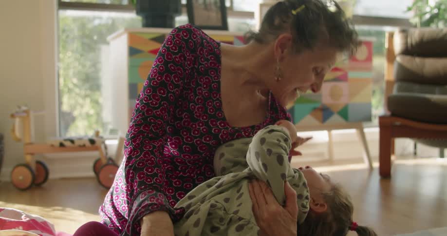 Grandmother playing and tickling granddaughter on the living room at home