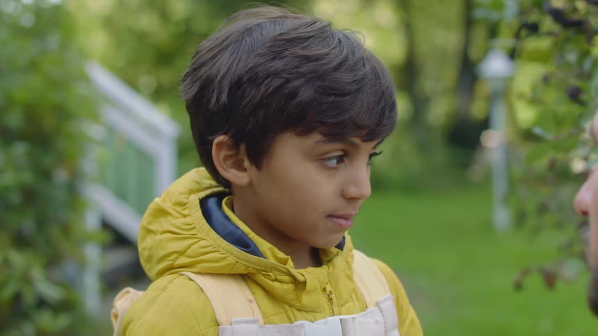 A boy is standing in a yard talking to a man