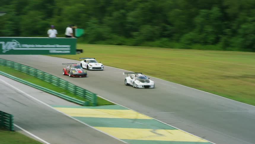 Cars race around a track as a man waves a green flag