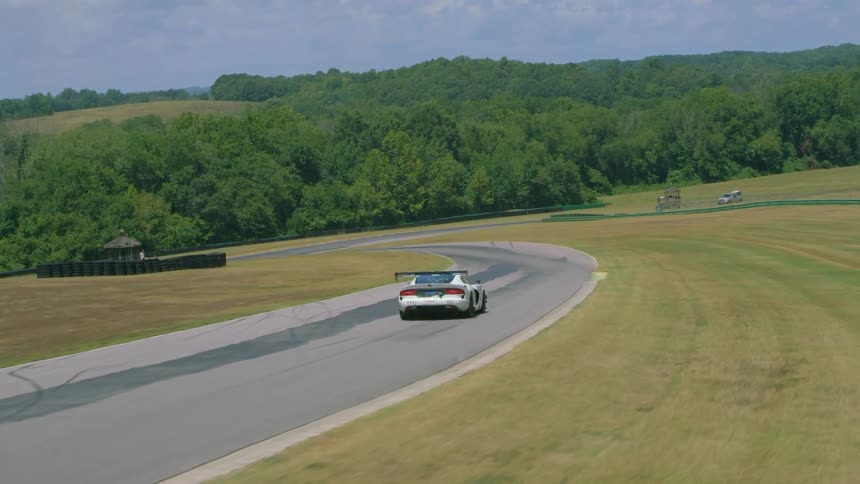 A number of race cars travel around a curved race track that is built atop a large grassy area