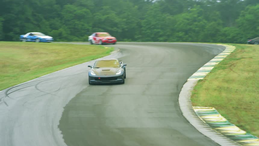 A sports car speeds around the curves of a racetrack with other vehicles trailing behind