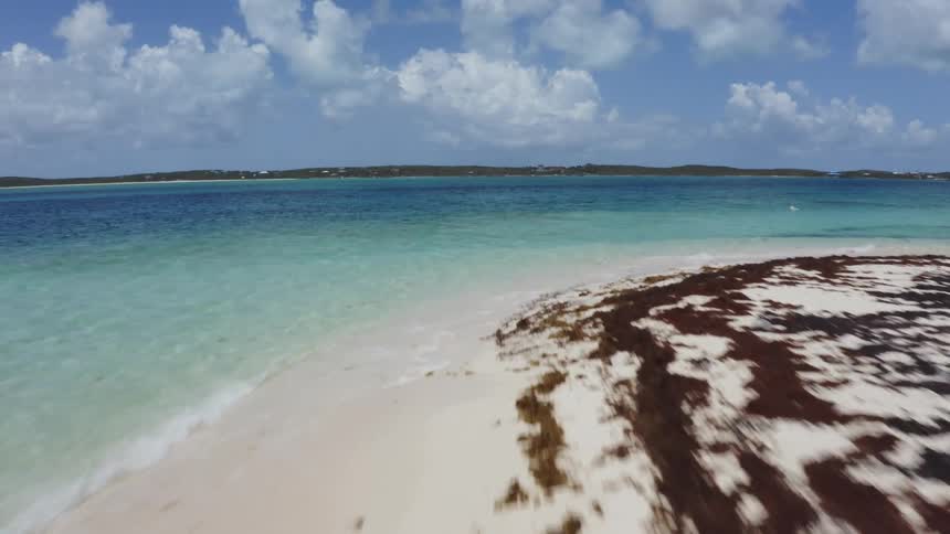 The camera soars quickly over an inviting looking beach lined with beautifully clear ocean water