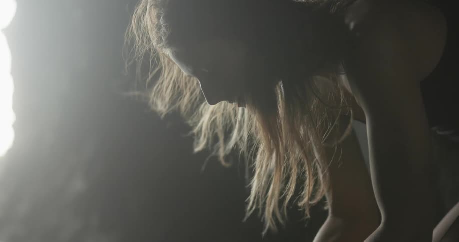 A woman with wind blowing through her hair with a spotlight in the background