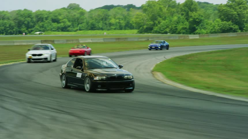 Several sports cars are speeding around a bend in a racetrack on a sunny day