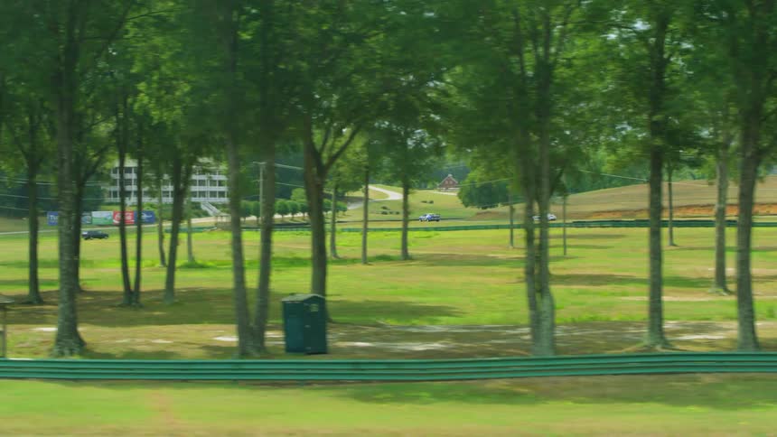 Two cars race on a racetrack near the trees