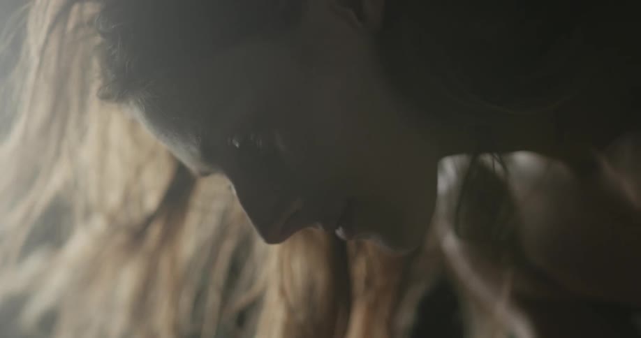 A womans hair blows around her as she stands with her upper body bowed