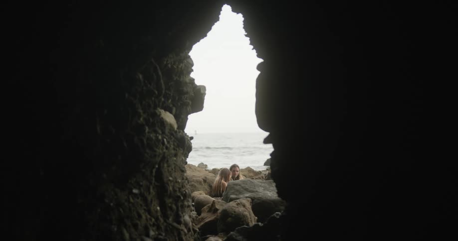 Young couple sitting at the entrance of a cave near the ocean at sunset