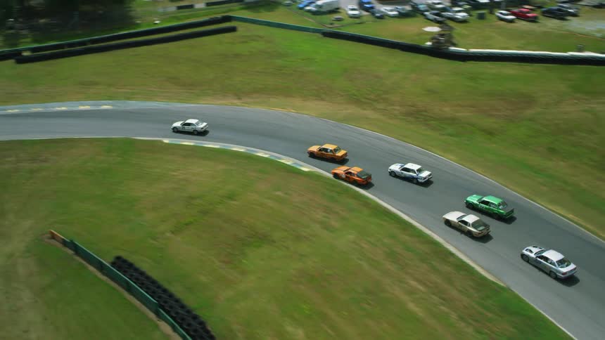 Cars race around a race track in a field on a sunny day