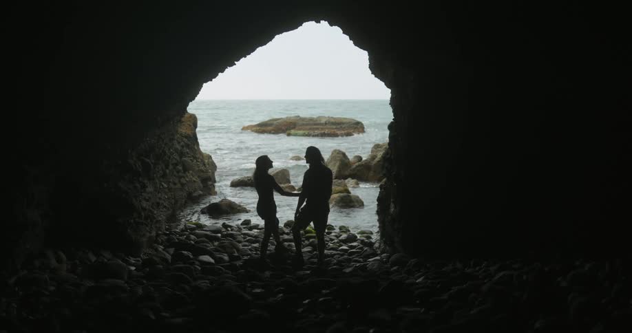 A man and woman stand in a cave by the ocean
