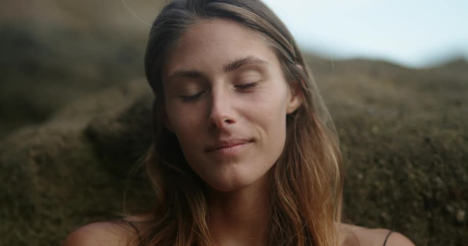 A woman is sitting outside and smiles and closes her eyes