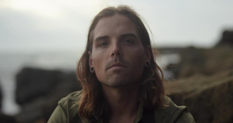 A man is posing by the rocks on the shore