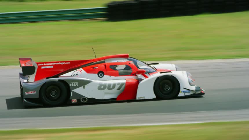Race cars race on a track near a forest and a field