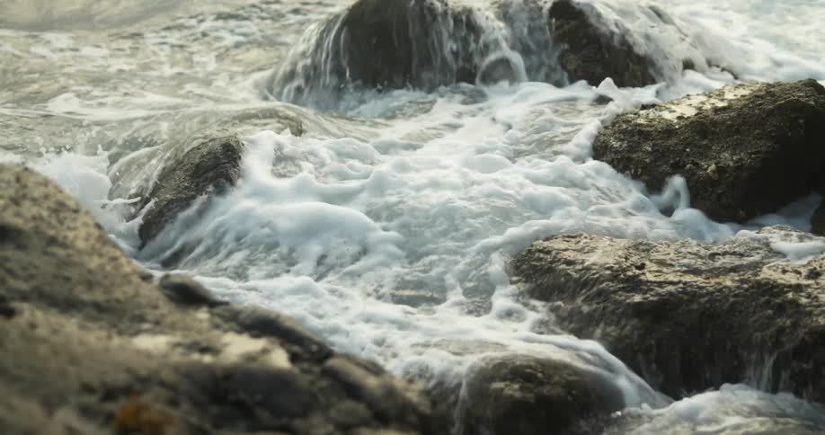 Small ocean waves crashing on the rocks in the coast of a beach at sunset