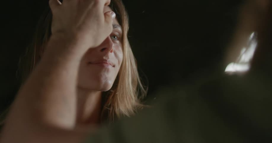 A man put in his hand through a womans hair in a cave with the sky and clouds in the background