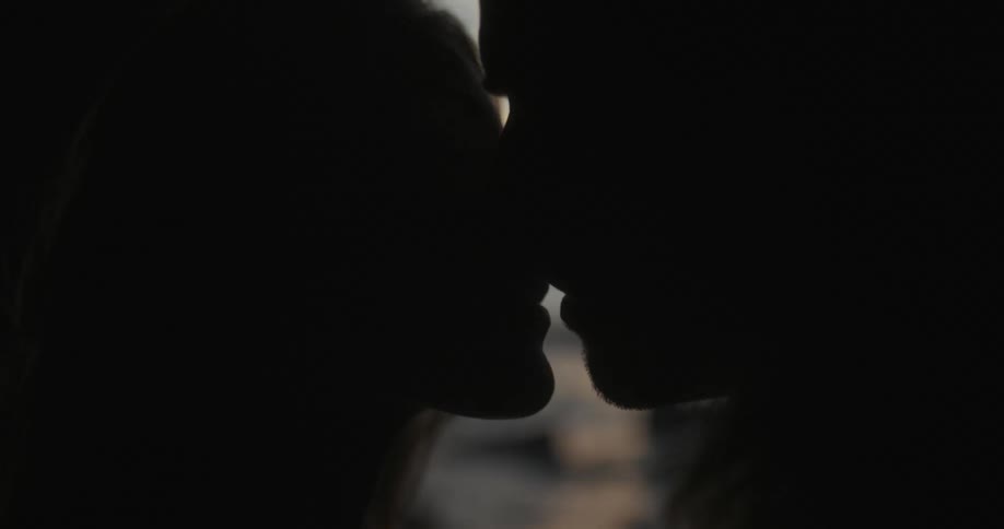 Couple kiss silhouetted by light coming through opening showing ocean and horizon