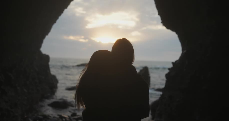 A boyfriend and girlfriend hugging next to the ocean in a cave