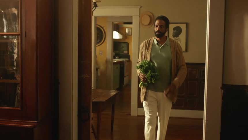 A man walking in a room holding a vegetable with a doorway and a wall in the background