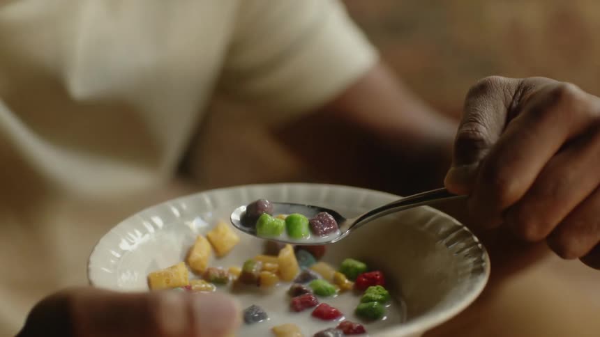 A man in a room eating cereal in a bowl with milk with a spoon