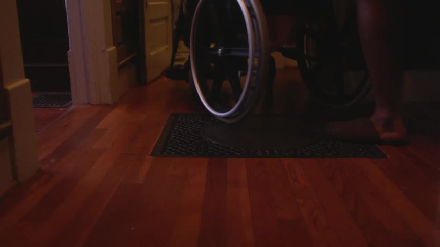 A person pushing another person in a wheelchair out of a hall and into another room