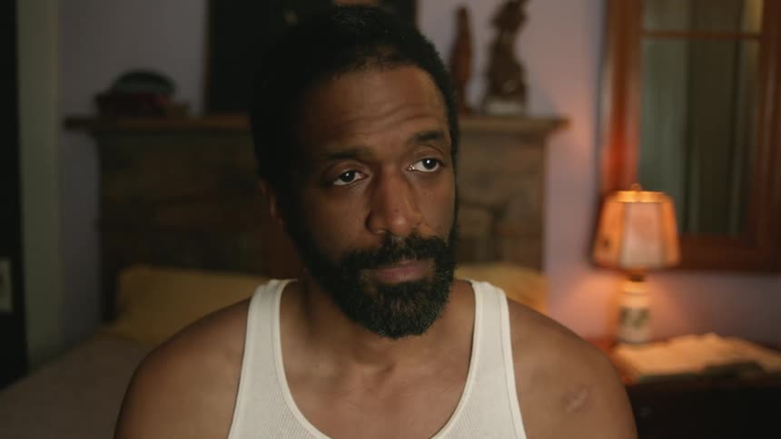 A man sits on the edge of his bed and watches television