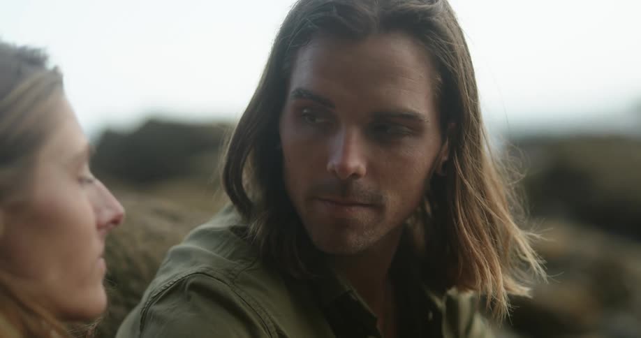 Man with long hair and green jacket looks at his girlfriend