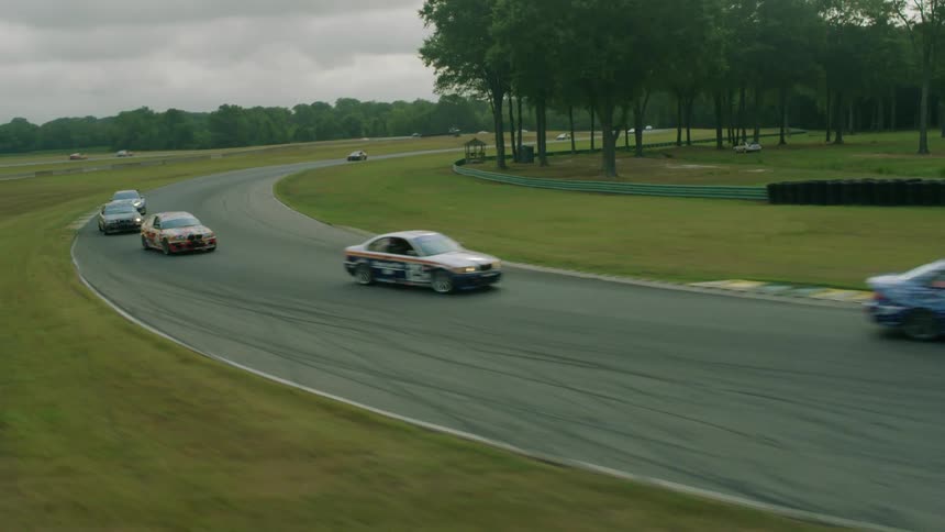 Race cars travel on an outdoor track with grass infield