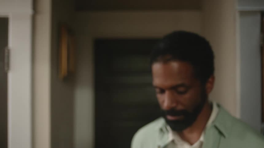 A man in a room with a door a picture frame and a wall in the background