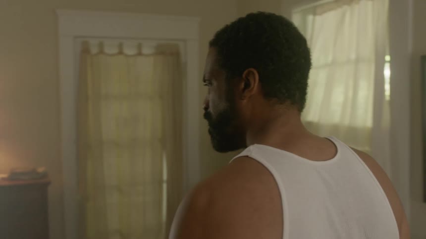 A man getting out of bed and grabbing a statue off a nightstand