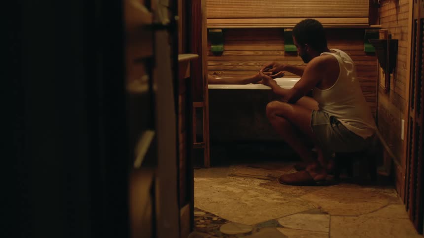 A man knees beside a bath tub and washes a womans hand as she lies in the tub