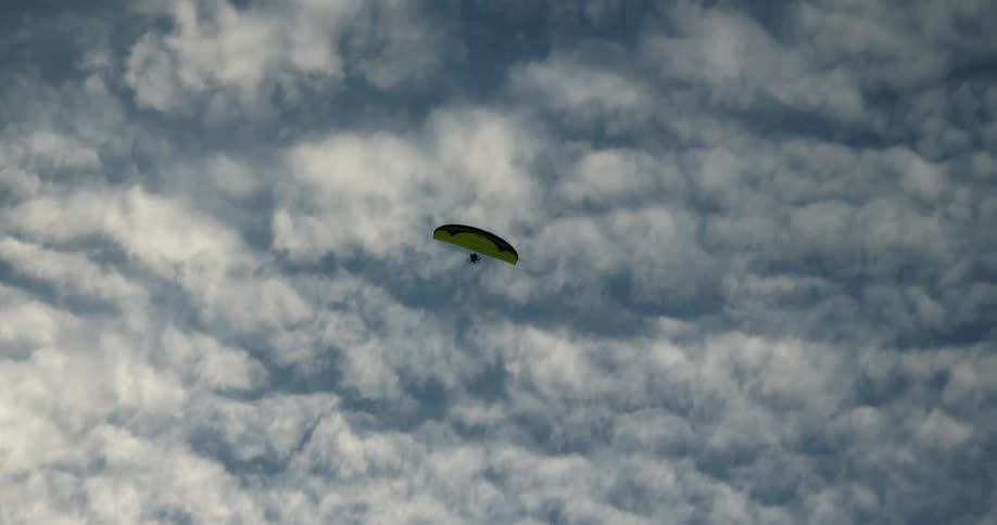 Person parasailing under the white clouds and blue sky
